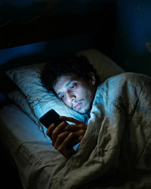 Rapaz na cama de madrugada, com o rosto iluminado pela tela